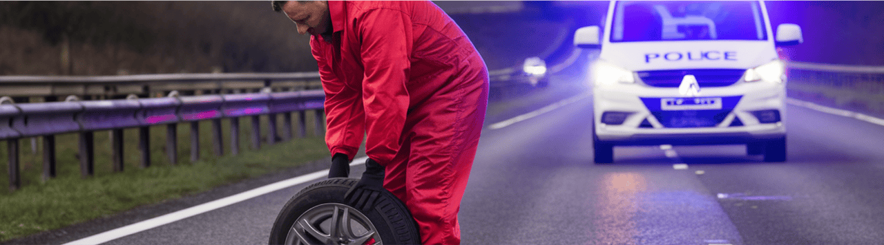 A man changing a tyre on a motorway with police car in background.