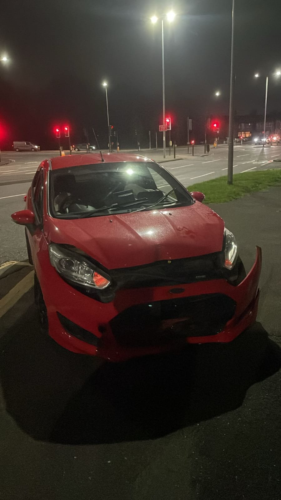 Front-end damaged car awaiting roadside recovery at night near Golborne.
