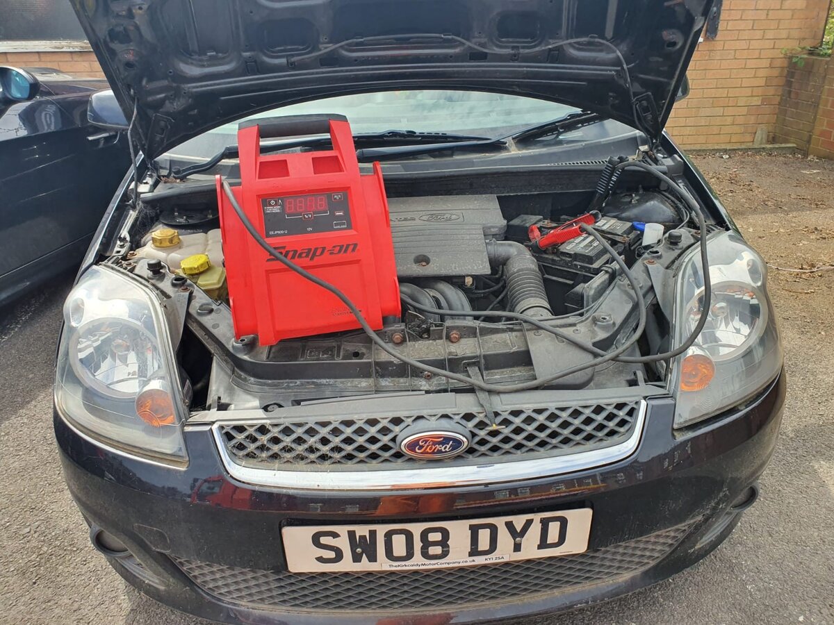 Black Ford Fiesta with a red Snap-on jump pack connected under the bonnet during a flat-battery jump start.