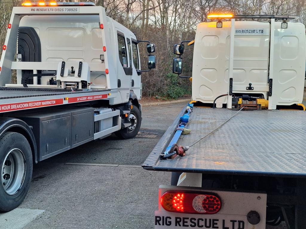 Red Breakdown Man recovery truck reversing onto a narrow rural lane to recover a blue saloon parked off the verge in the trees