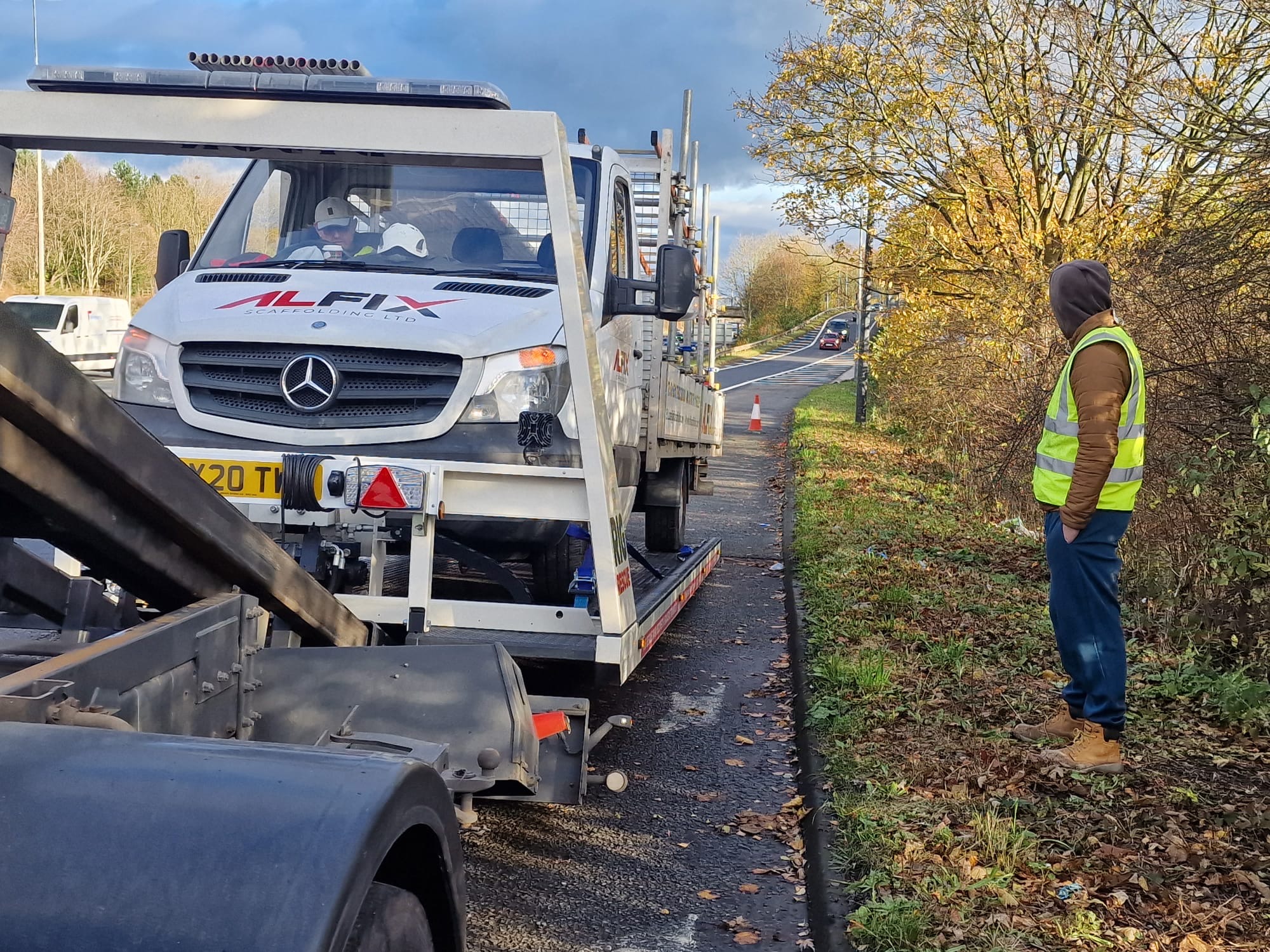 Breakdown Man Iveco Daily recovery truck DG64 YME parked at a coastal yard alongside a white Isuzu lorry with the operator beside the cab