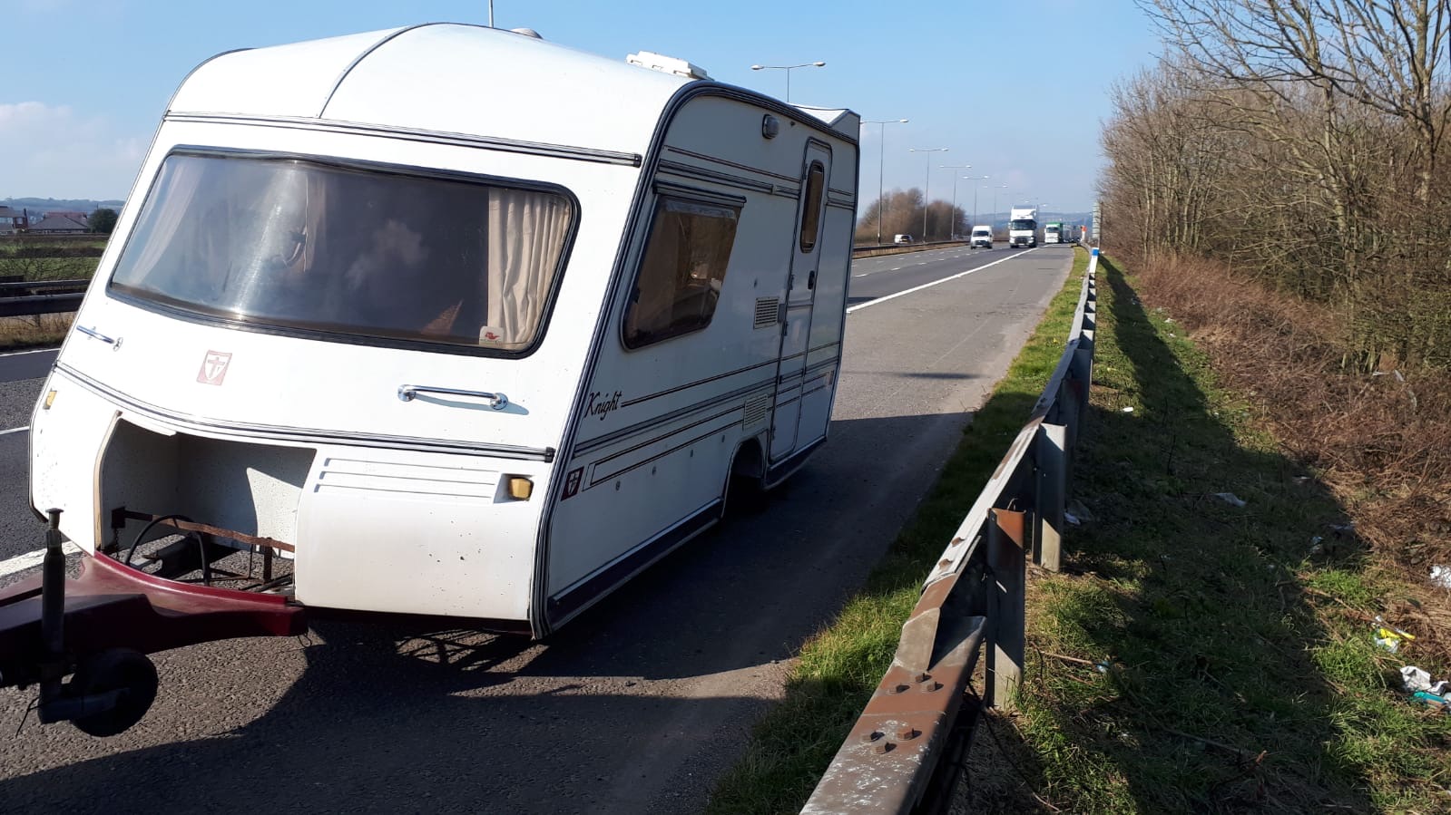 A caravan loaded on a recovery trailer on a dual-carriageway hard shoulder, ready for transport to safety