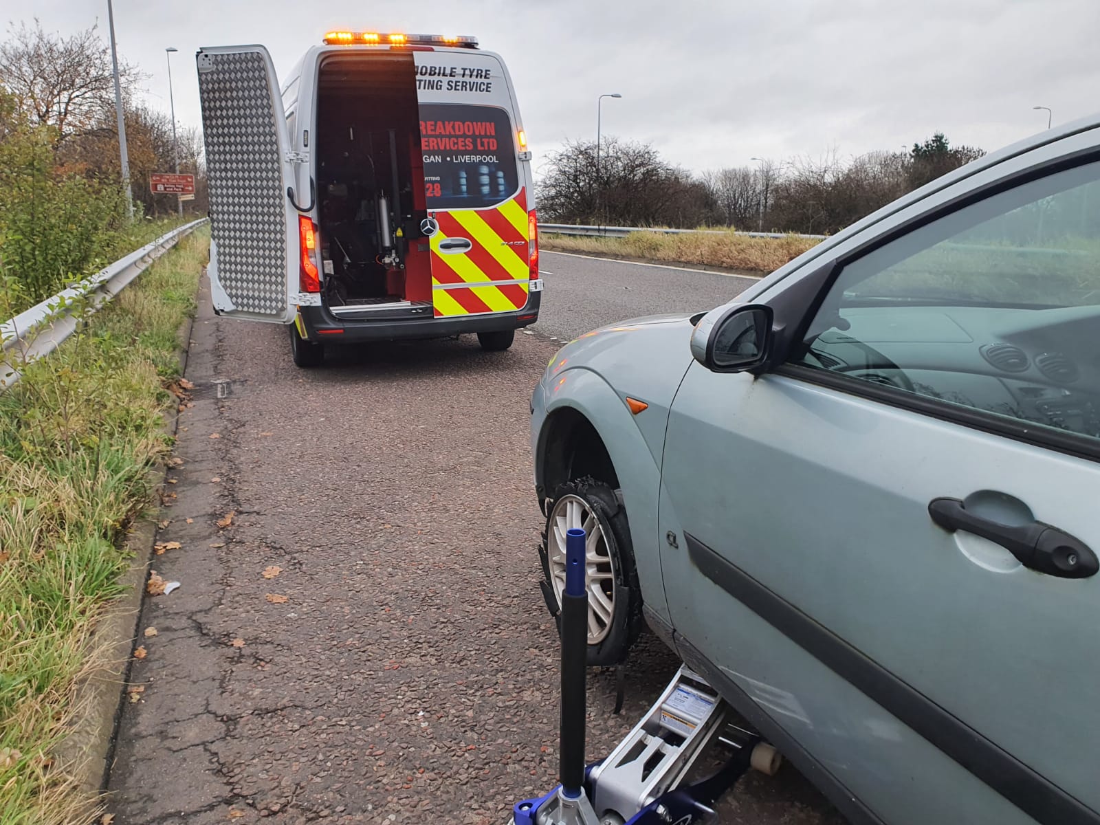 Breakdown Man mobile tyre fitting van at the roadside, changing a car tyre with a trolley jack