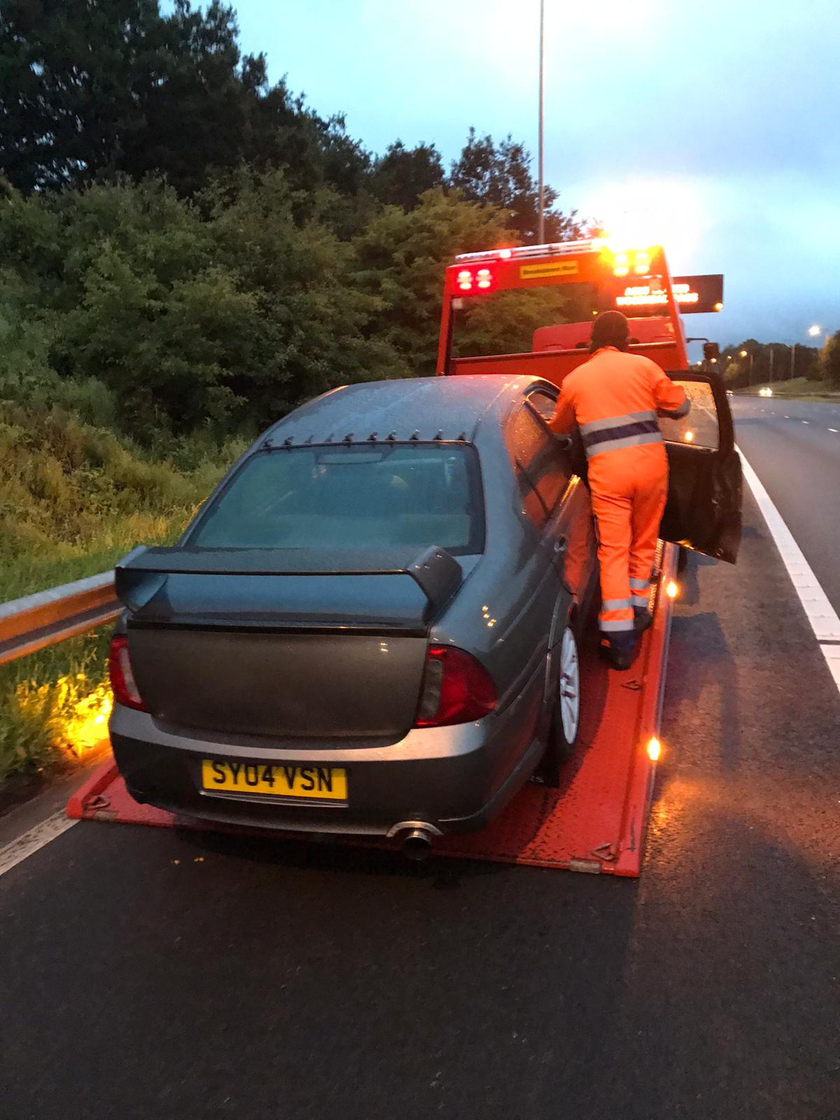 White Toyota Prius being recovered onto the Breakdown Man recovery truck beside the SOS 1376A emergency phone on the M62 hard shoulder