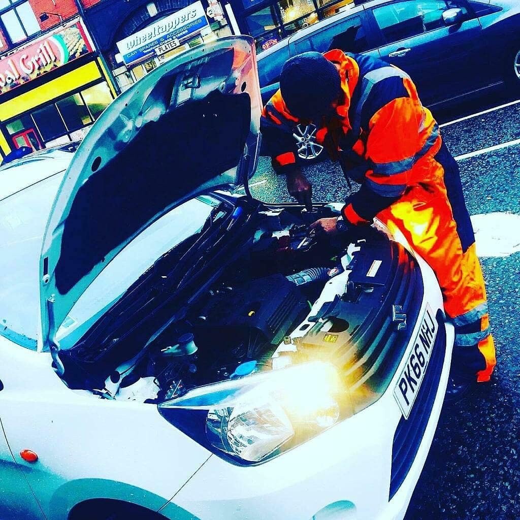 Breakdown Man operator in hi-vis performing a jump start under the bonnet of a white car at the roadside.