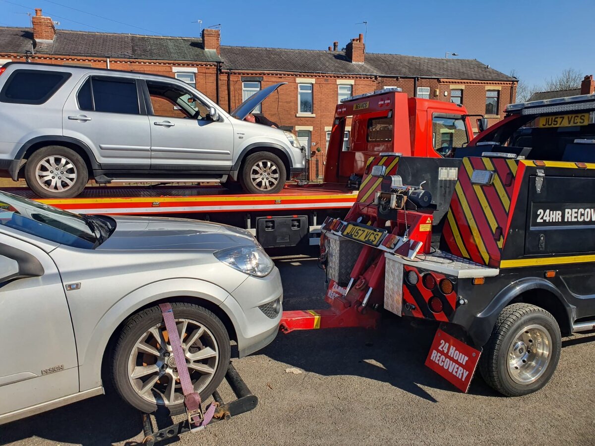 Breakdown Man 24-hour recovery truck loading a silver Honda CR-V on a terraced street.
