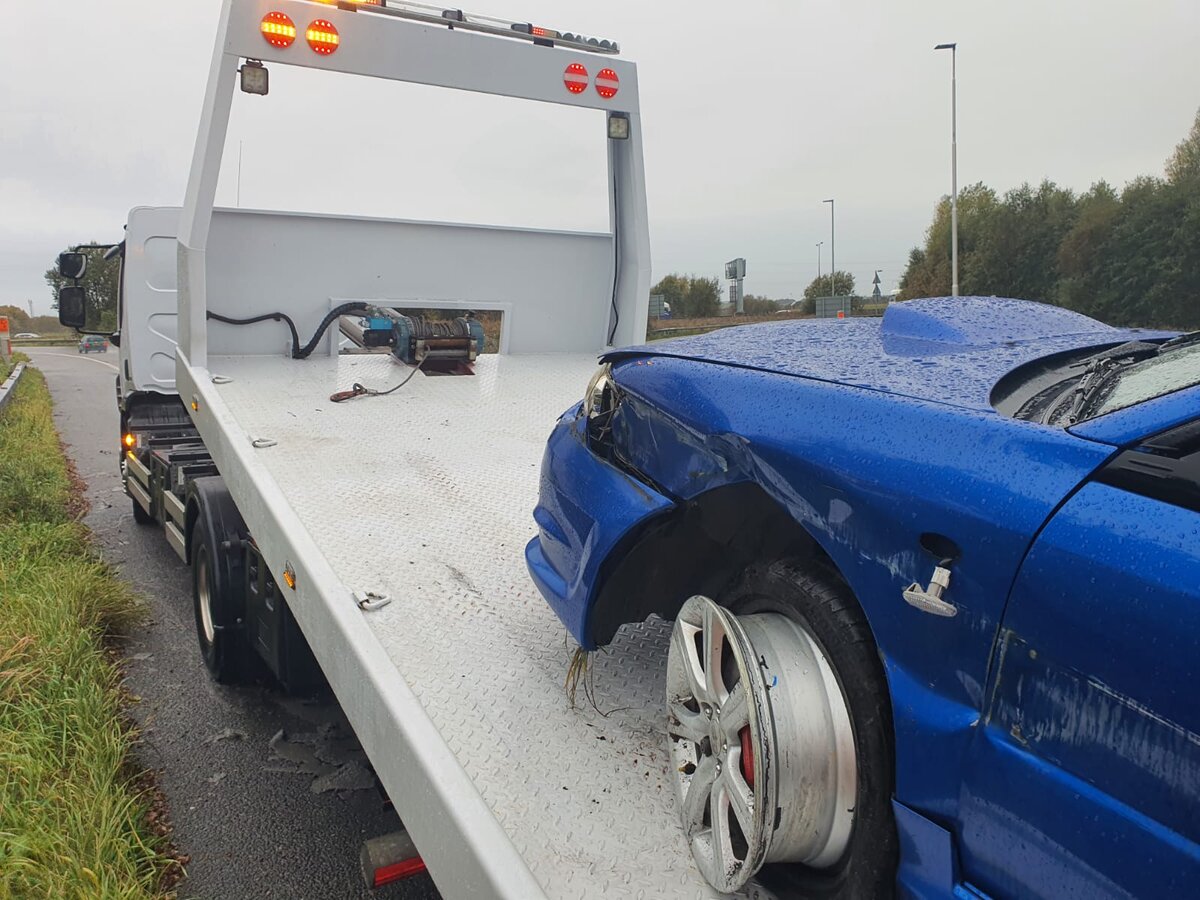Accident-damaged blue Subaru Impreza loaded onto a white flatbed recovery truck after a side impact.