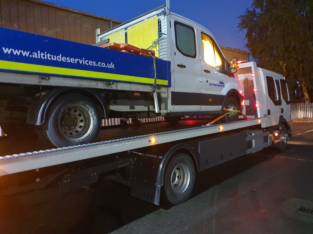 Altitude Services white Ford Transit dropside being recovered on Breakdown Man's flatbed at night.