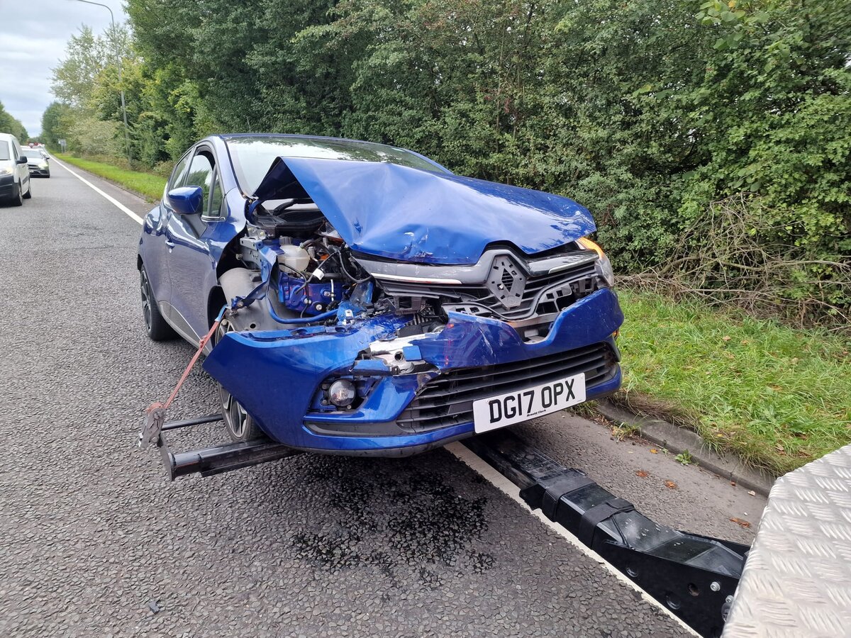 Crash-damaged blue Renault Clio DG17 OPX on recovery skates at the roadside after a front-end collision.