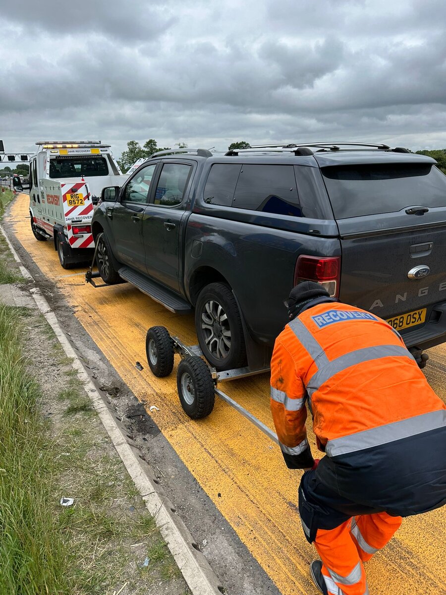 Black Ford Ranger pickup loaded on Breakdown Man's flatbed, hi-vis crew strapping it down on the hard shoulder.