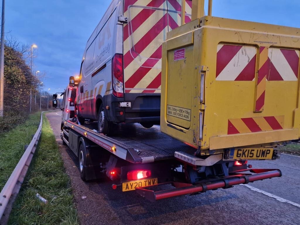 Gough & Kelly silver Iveco van strapped down on Breakdown Man's flatbed at dusk on the motorway slip road.
