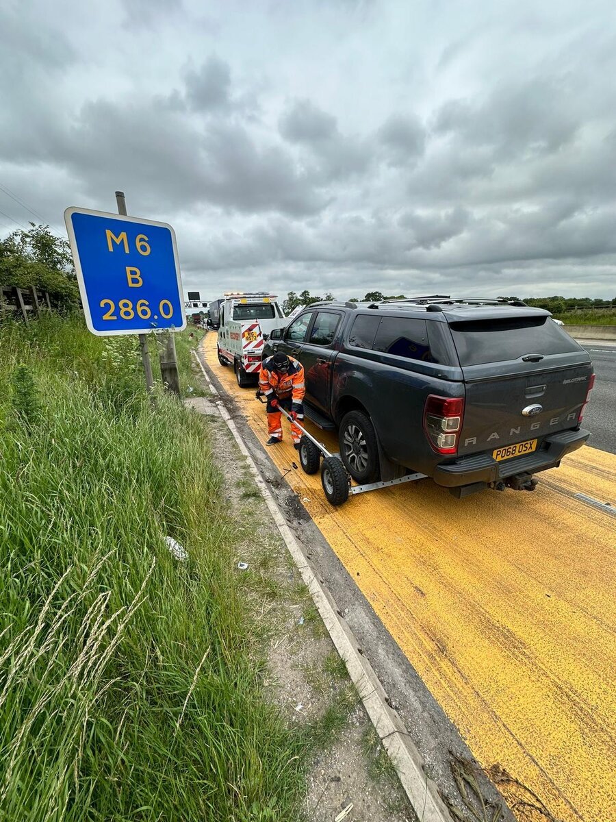 Breakdown Man recovery operator securing a grey Ford Ranger Wildtrak to the flatbed beside the M6 hard shoulder.
