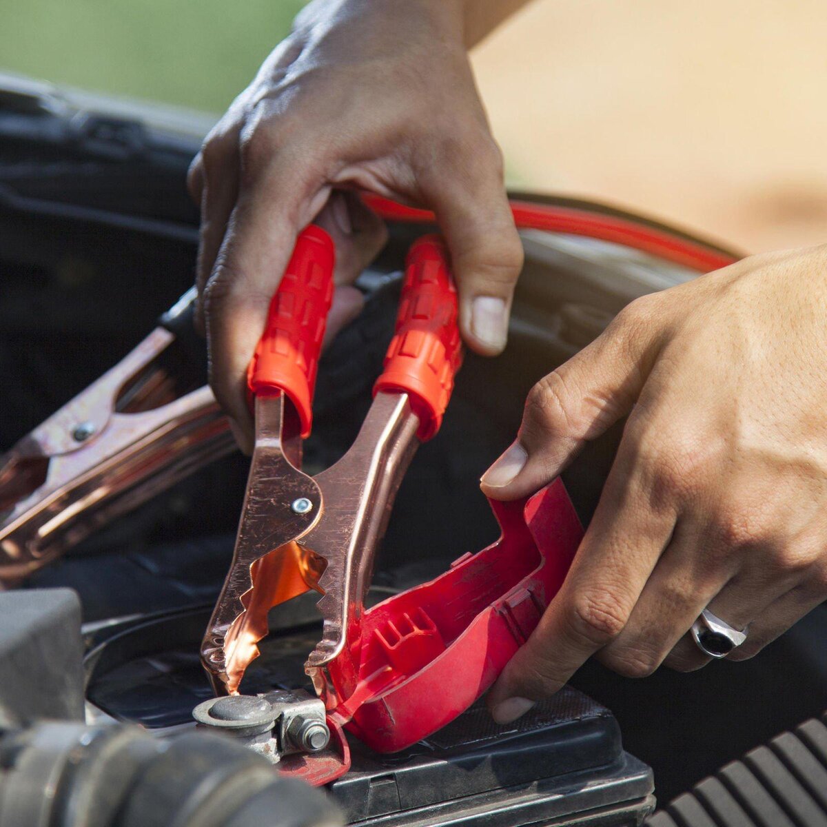 Close-up of red and copper jumper-cable clamps connecting to a car battery terminal during a jump start.