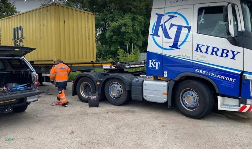 Kirby Transport blue Volvo HGV being attended for a flat-battery jump start at the depot.