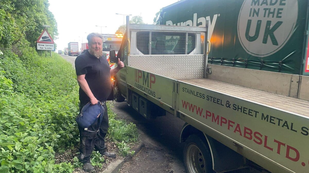 PMP Fabrications stainless-steel flatbed truck stopped on a country road with the driver awaiting Breakdown Man recovery.