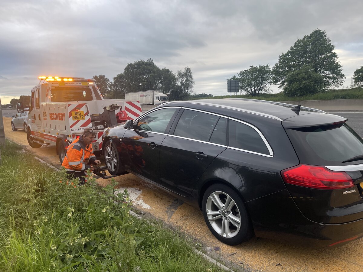 Black Vauxhall Insignia estate on the motorway grass verge, Breakdown Man crew fitting front-end skates ready to tow.