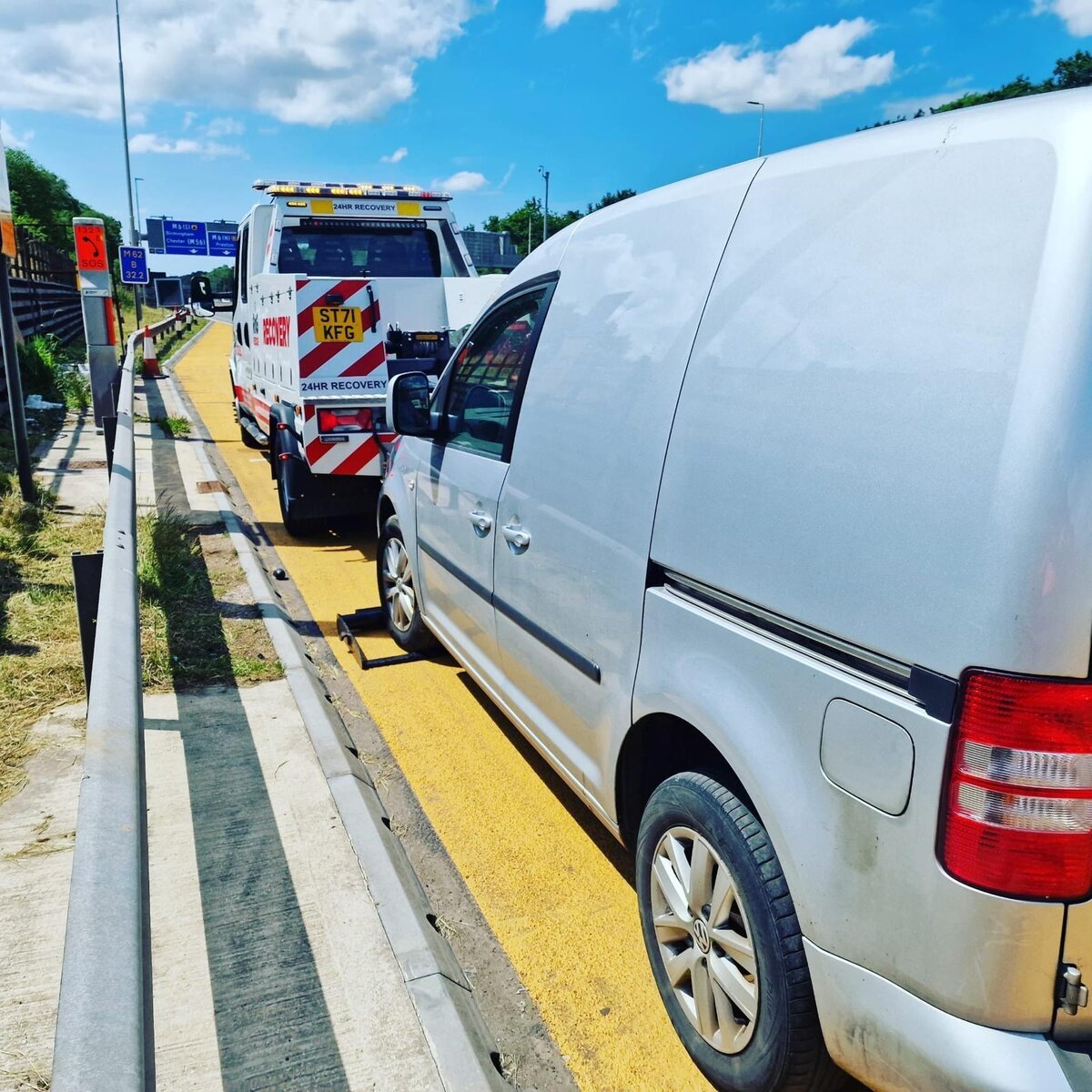 Breakdown Man recovery truck ST71 KFG with a silver VW Caddy van loaded on the flatbed at a motorway sliproad.