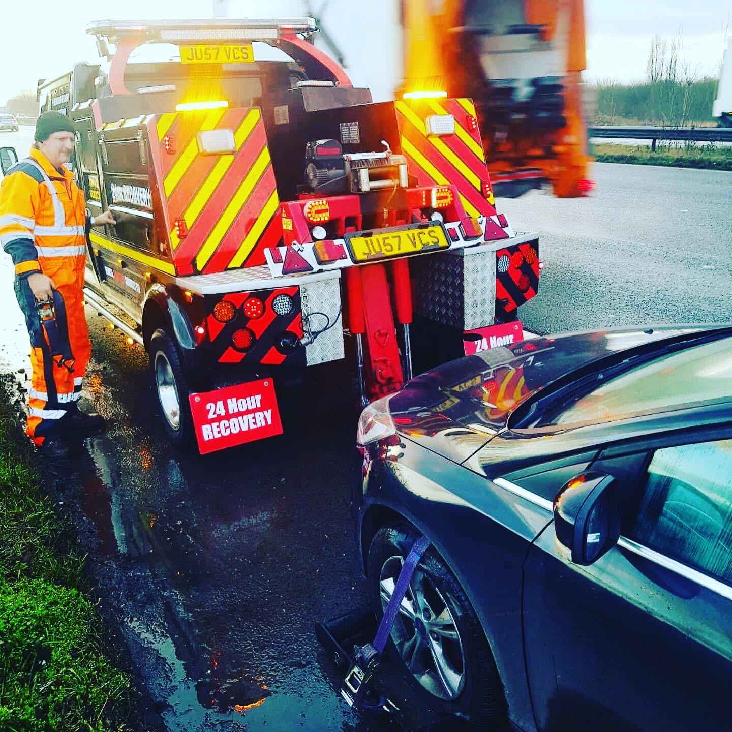 Breakdown Man operator in hi-vis beside the recovery truck with a customer's car secured on the bed at the roadside.