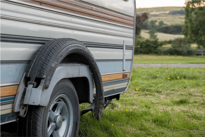 Old worn down caravan with a flat tyre.